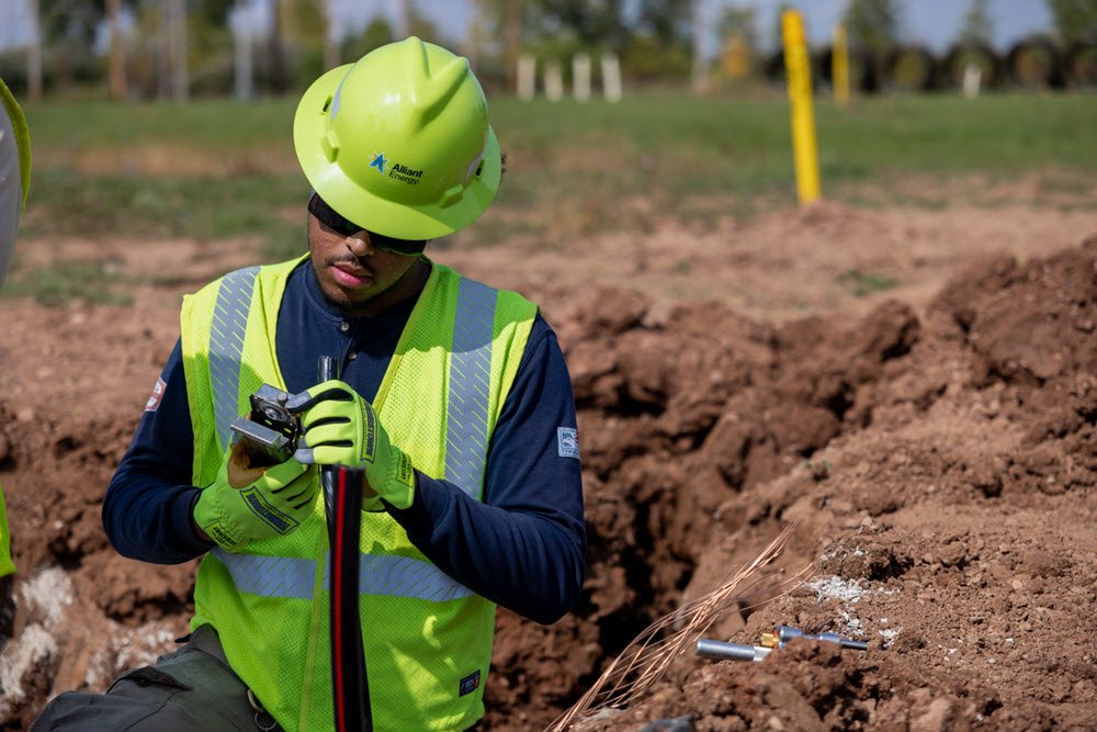 Worker in a hard hat, safety vest and glasses inspecting an underground power line. 