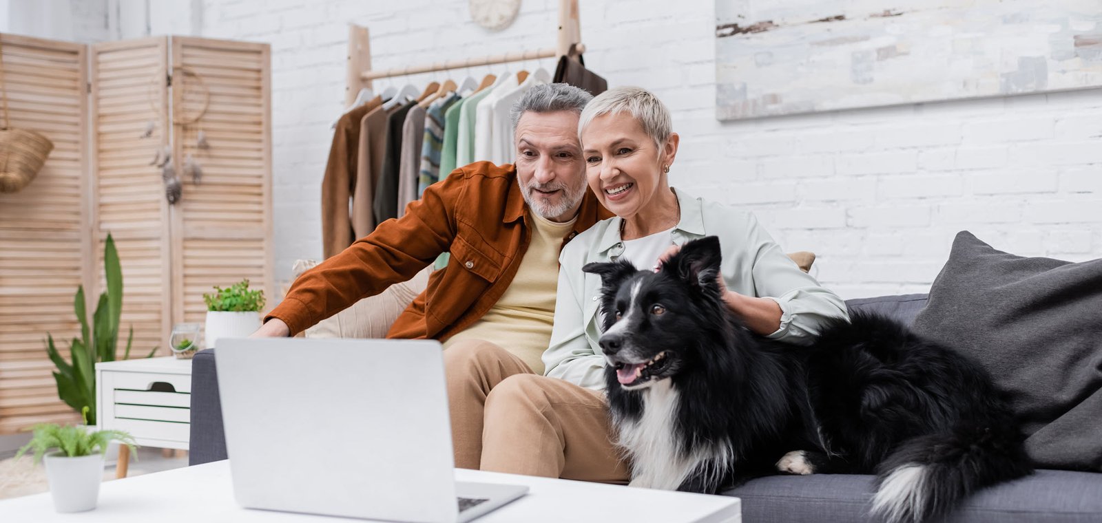 couple looking at a laptop on a couch with their dog